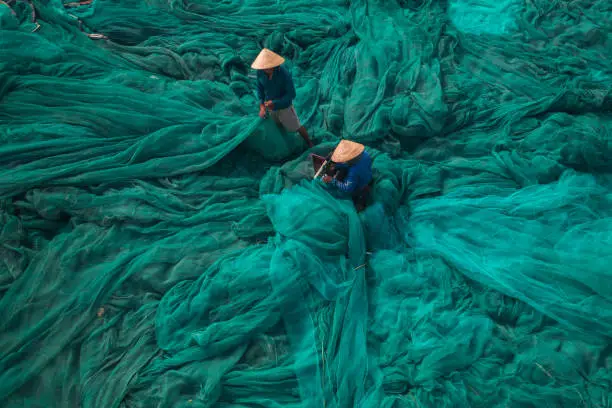 High angle view of 2 men is knitting fishing net on a large beautiful turquoise fishing net by the beach in Van Ninh town, Khanh Hoa province, central Vietnam