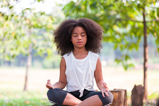 African American little girl doing meditate yoga asana with eyes closed outdoor in park. Kids girl practicing doing yoga outdoor