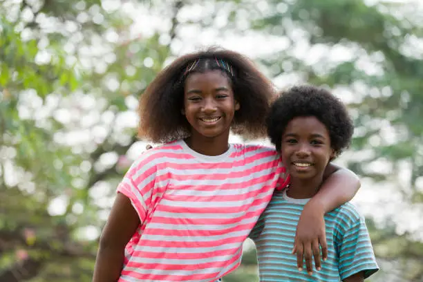 Photo of Smiling African American boy and girl playing and hugging together outdoor. Happy afro kid having fun or enjoying together in the park. Happy black people. Education and field trips concept