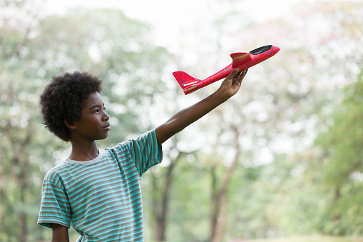 African American boy playing with toy airplane outdoor. Kid having fun with toy airplane in the park. Happy black people. Education and field trips concept