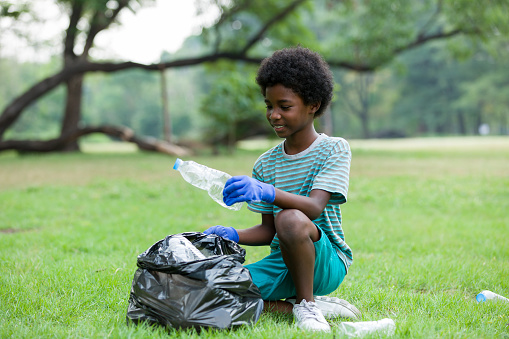 African American smiling boy holding black garbage bag with plastic bottle. Volunteer concept