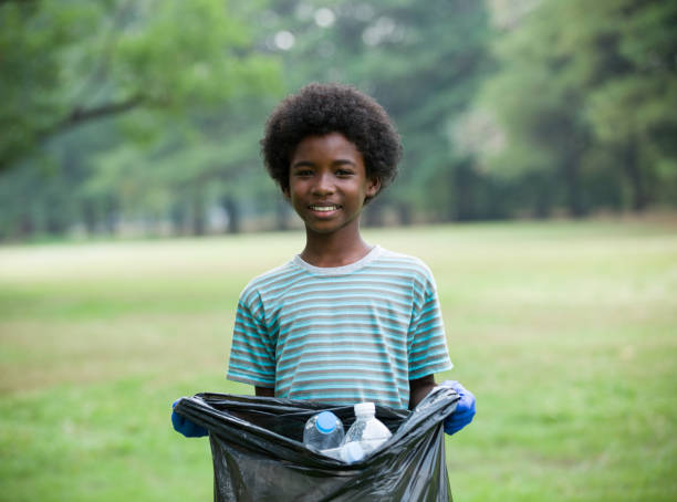 garçon afro-américain souriant tenant un sac poubelle noir avec une bouteille en plastique. concept de bénévolat - bag garbage bag plastic black photos et images de collection