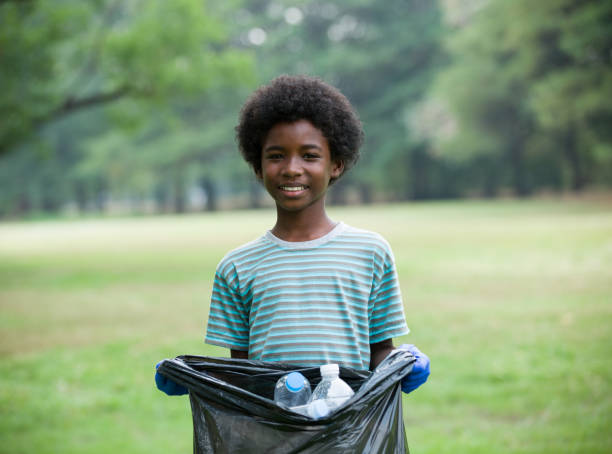 garoto afro-americano sorridente segurando saco de lixo preto com garrafa de plástico. conceito voluntário - bag garbage bag plastic black - fotografias e filmes do acervo