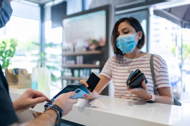 Woman With Protective Face Mask Paying With Contactless Card At Woman With Protective Face Mask Paying With Contactless Card At consumer confidence photos stock pictures, royalty-free photos & images