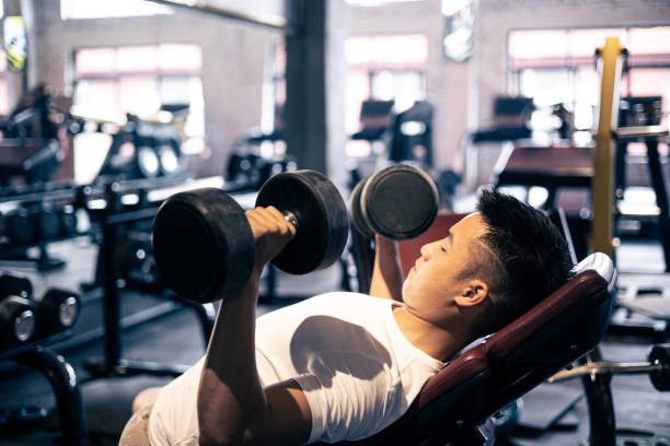 homme soulevant des haltères dans le gymnase - weight bench flash photos et images de collection