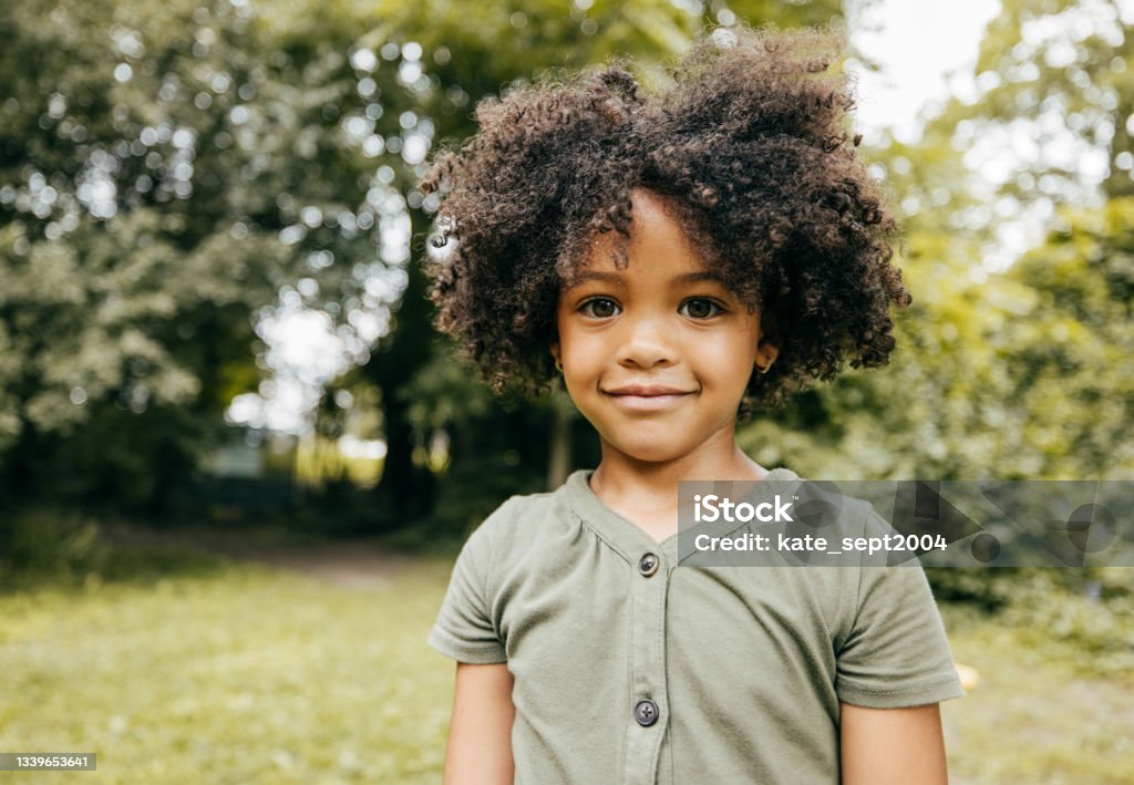 Connecting Kids and Nature Portrait of cute African-American girl smiling and looking at the camera while she is at the park. 4-5 Years Stock Photo