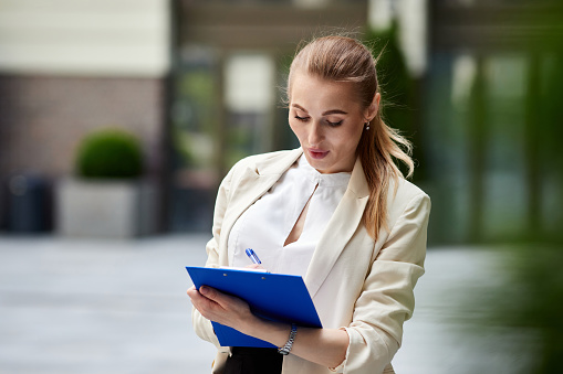 beautiful business woman with blue clipboard outdoors. copy space