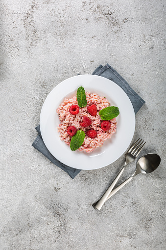 Risotto with raspberry fruits served in a white dish on a grey stone table. flat lay with copy space. Italian gourmet cuisine. Selective focus. Vertical orientation
