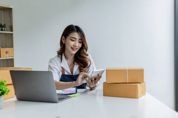 An Asian woman is pressing a white calculator, she owns an online store, she is using an order amount calculator to get a summary of the amount customers have to pay. Online selling concept. una mujer asiática está presionando una calculadora blanca, es dueña de una tienda en línea, está usando una calculadora de monto de pedido para obtener un resumen de la cantidad que los clientes tienen que pagar. concepto de venta online.