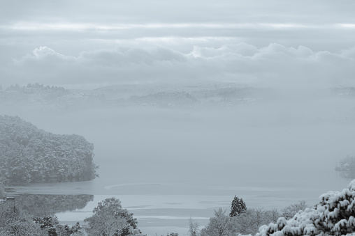 Early morning winter landscape at a fjord (Nordasvannet) near the City of Bergen on the west coast of Norway after snowfall. The seawater of the fjord is partly frozen and covered with snow. The image was captured on an overcast and cloudy day.