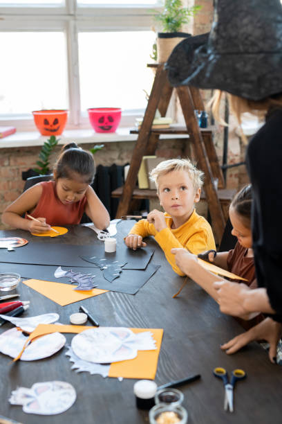 istock Cute serious boy looking at teacher in whitch hat 1339672963
