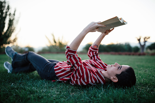 Young woman reading book in park (Analog book reader)