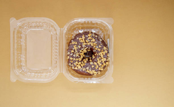 istock Chocolate donut in a plastic container on a brown or coffee background. Takeaway breakfast concept. One donut is packed in a plastic box for delivery. Sweet pastries delivered to your home. Top view 1339675282
