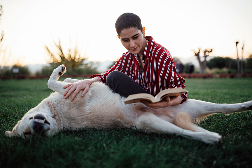 Young woman reading book in park with a lovely dog (Analog book reader)
