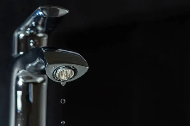 Clean water is dripping from the faucet on a black background.
