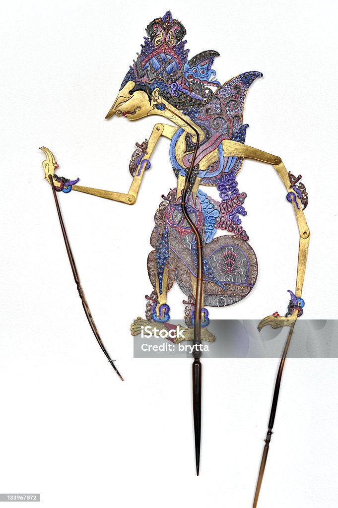Indonesian traditional Wayang Kulit  puppet hanging on white wall Indonesian flat wayang shadow puppet hanging on a white textured wall.The puppet is made of leather and is carefully chiseled.The handles and control rod are made of buffalo horn. Puppet Stock Photo