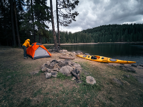 Setting up tent for camping on a mountain lake shore on a bright sunny day.