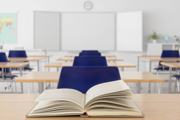 open book on wooden desk with blurred empty classroom background. - ausência imagens e fotografias de stock