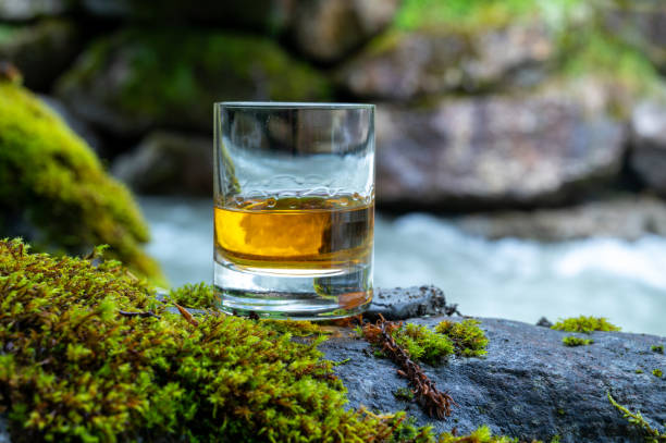 glass of strong scotch single malt whisky with fast flowing mountain river on background - spey scotland stockfoto's en -beelden