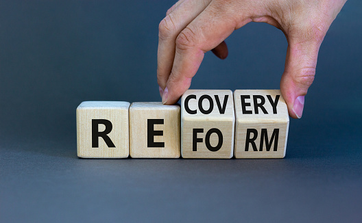 Recovery and reform symbol. Businessman turns cubes and changes the word 'recovery' to 'reform'. Beautiful grey background. Business and recovery - reform concept. Copy space.