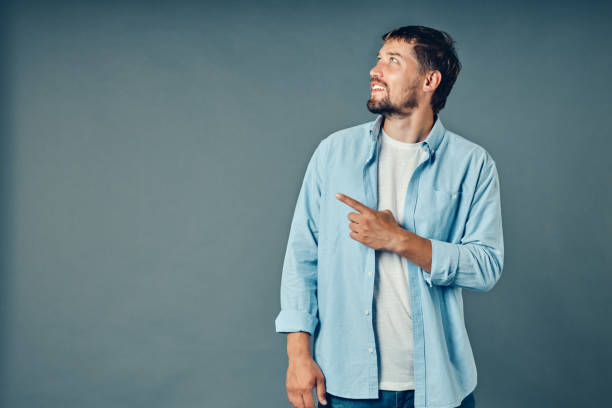 istock A young Caucasian guy with a beard smiles and points his finger to the side of the empty space 1339682420