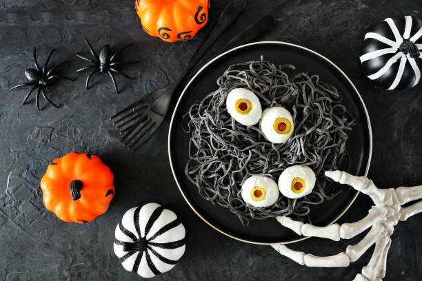 Halloween eyeball spaghetti. Top view table scene over a dark background with orange, black and white decor. Healthy black bean pasta.
