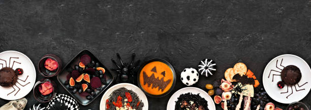 Halloween dinner party bottom border over a dark black banner background Halloween dinner party bottom border over a dark black banner background. Top view. Spooky charcuterie board, black risotto and pasta, spider cakes, jack o lantern pumpkin soup, and apple skull wine jack o lantern photos stock pictures, royalty-free photos & images