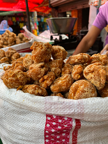 Stock photo showing a close-up view of pieces of jaggery in large sacks being sold by a market trader from outdoor stall display. This produce is used as a 'healthy' alternative to sugar.