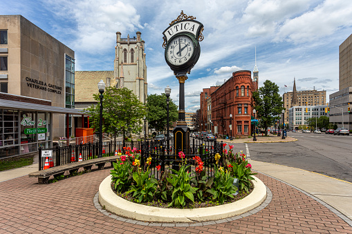 Utica, New York, USA — August 3, 2021: Floral plantings and a street clock welcome visitors to the central downtown district of Utica, New York.