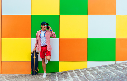 a man on a skateboard, talking on the phone while leaning against a colorful wall.