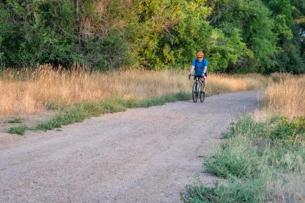 senior male cyclist is riding a touring bike on a gravel trail along the Poudre River in Fort Collins, Colorado, late summer scenery