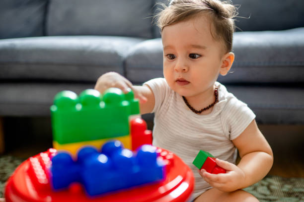 Cute toddler develops motor skills by playing with toy blocks at home Cute toddler develops motor skills by playing with toy blocks at home motor skills in babies stock pictures, royalty-free photos & images