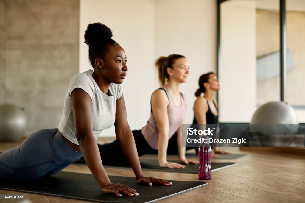 Black female athlete doing stretching exercises while warming up with group of women at health club. Athletic women doing stretching wile exercising on group training in a gym. Focus is on African American woman. Exercising Stock Photo