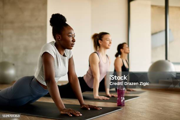 Black Female Athlete Doing Stretching Exercises While Warming Up With Group Of Women At Health Club Stock Photo - Download Image Now