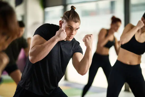 Muscular build man practicing martial arts while working out with group of people at health club