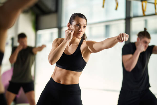 Young sportswoman exercising hand punches during martial arts training at health club. Female martial artist practicing punches while having exercise class at health club. martial arts photos stock pictures, royalty-free photos & images