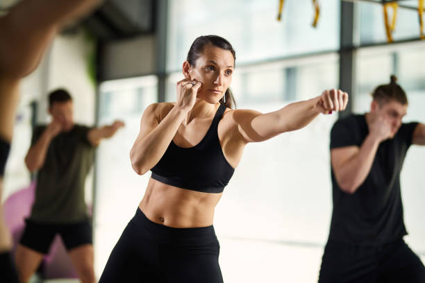 Young sportswoman exercising hand punches during martial arts training at health club. Female martial artist practicing punches while having exercise class at health club. combat sport stock pictures, royalty-free photos & images