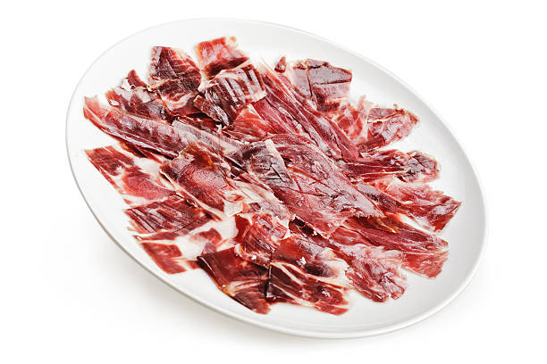 Slices of ham cutted by hand on a white plate over a white background