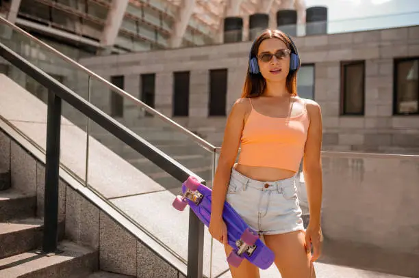 Leisure. A cute young woman iwith a skateboard and headphones looking positive