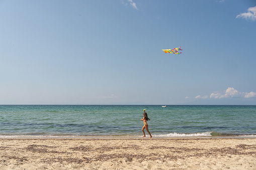 Adorable girl, running on the beach while holding the kite, who flying on the wind