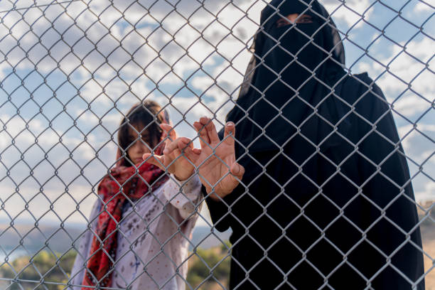 Refugee woman and daughter standing behind a fence Refugee woman and daughter standing behind a fence deportation stock pictures, royalty-free photos & images