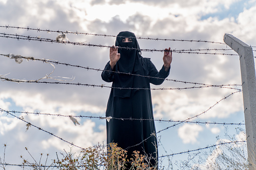Refugee woman standing behind a fence