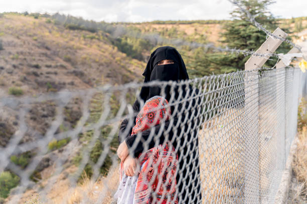 Refugee woman and daughter standing behind a fence stock photo