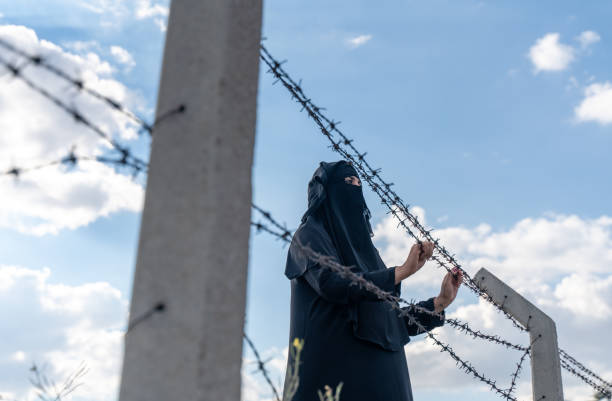 istock Refugee woman  standing behind a fence 1339716712
