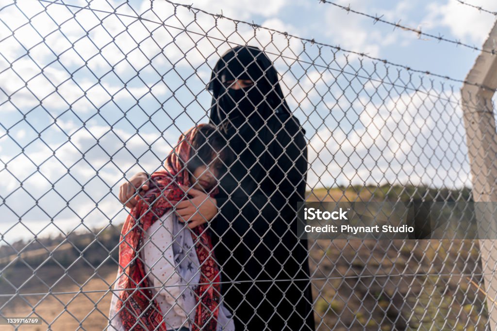 Refugee woman and daughter standing behind a fence Refugee Stock Photo