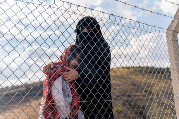 Refugee woman and daughter standing behind a fence stock photo