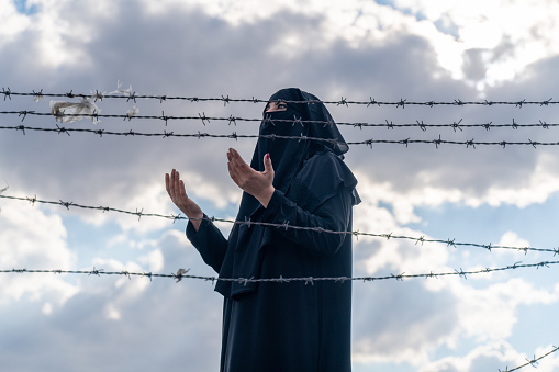 Refugee woman  standing behind a fence  praying