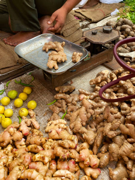 istock Image of unrecognisable market trader using weighing scales to sell fresh ginger root (Zingiber officinale) from outdoor fruit and vegetable market stall, focus on foreground 1339724242
