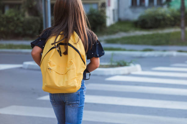 School girl with yellow school bag on a crosswalk stock photo