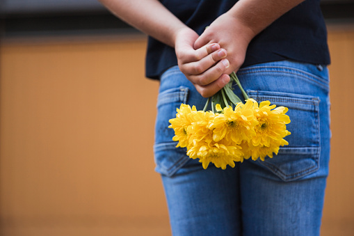 Young child hiding bouquet of freshly picket yellow flowers behind her back to surprise her mother